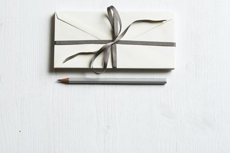 White envelope wrapped with grey ribbon in a bow and pencil