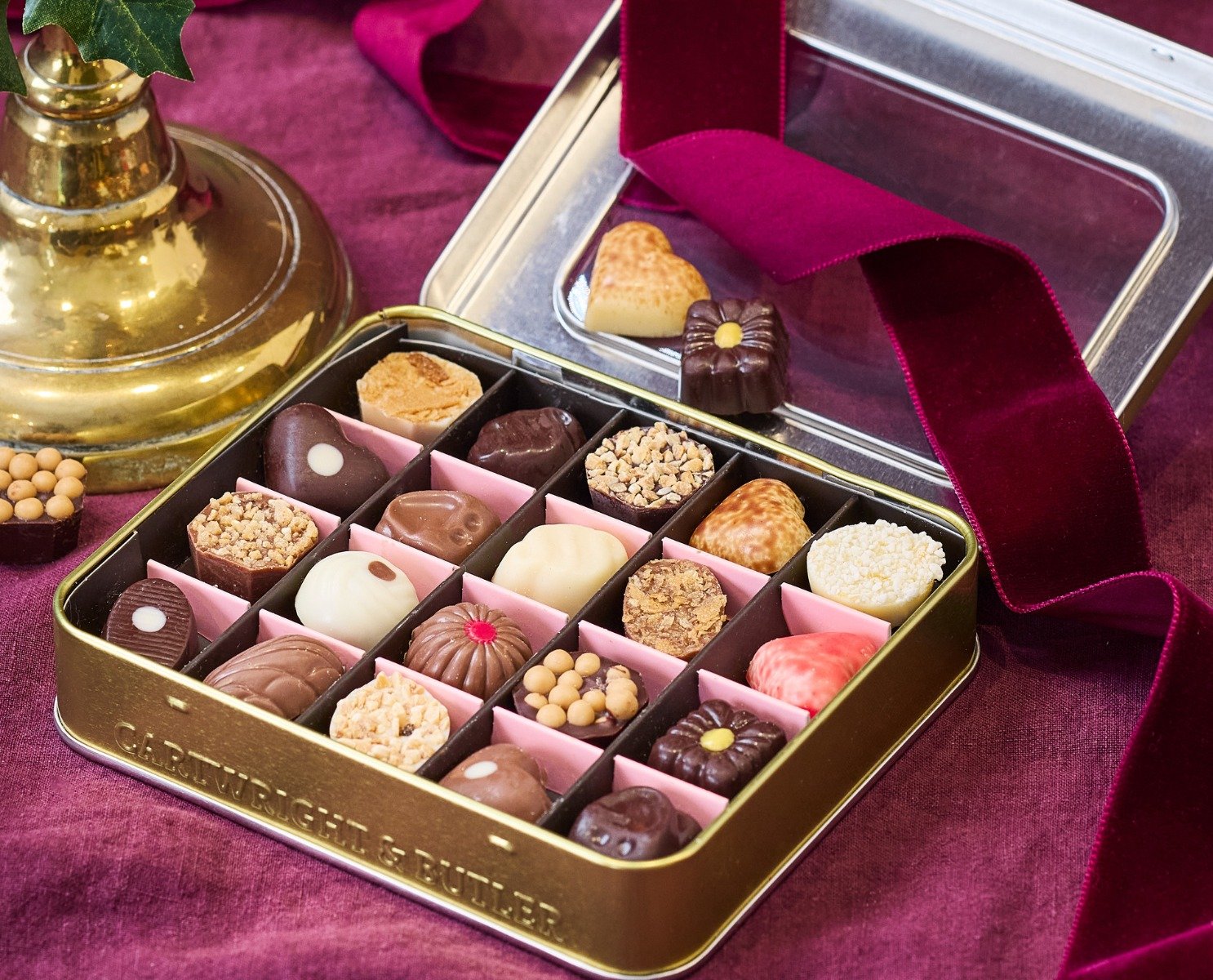 Open box of rich Belgian chocolate box with gold tray , a velvety dark burgundy ribbon sitting over the lid