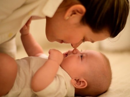 Baby laid down with mum hovering over for a kiss