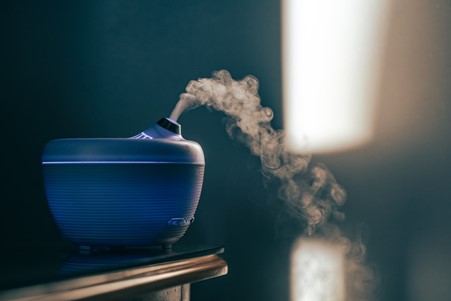 Blue aromatherapy diffuser sat on a wooden table puffing out scent 