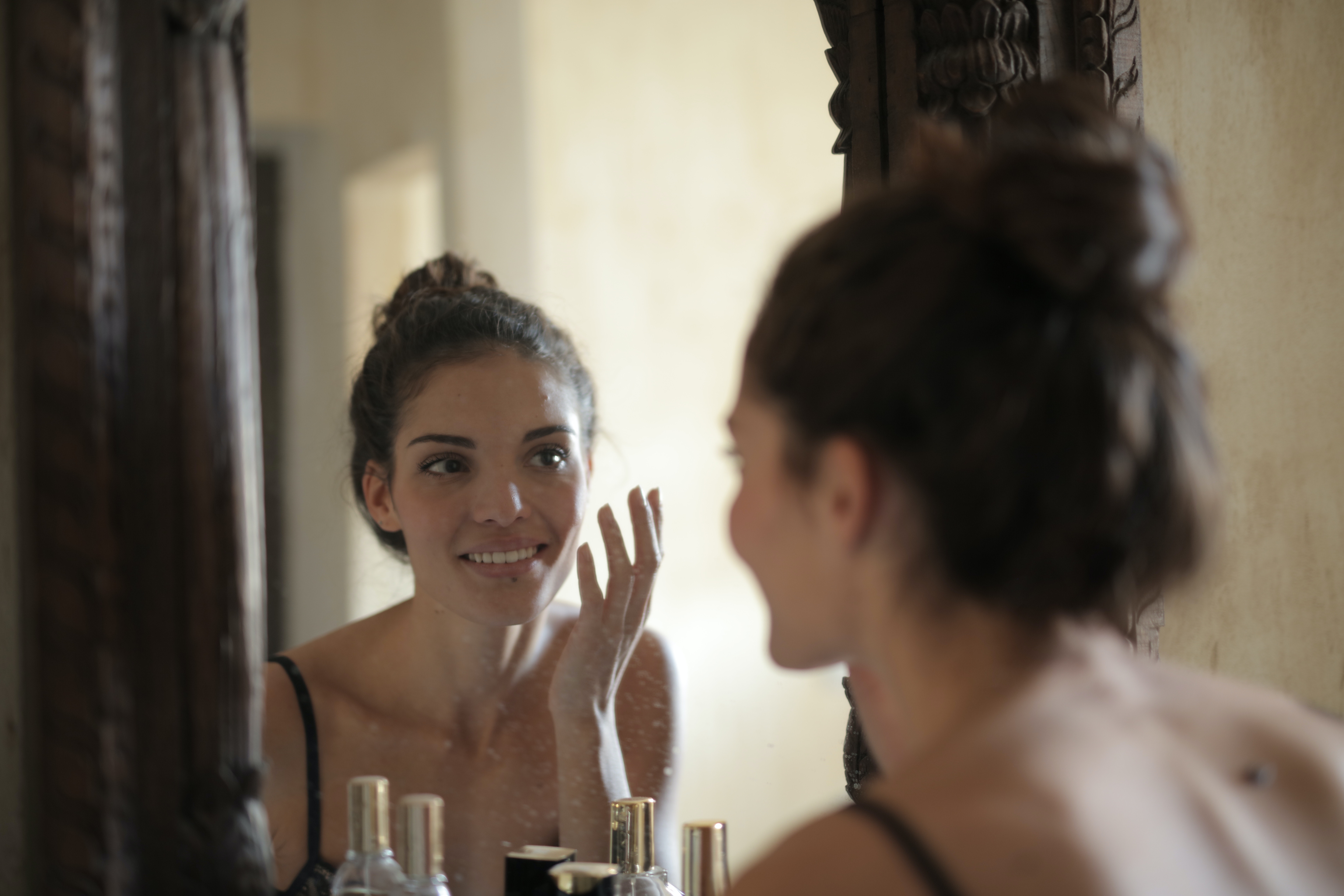 Reflection of woman with brown hair doing skin care routine with hand