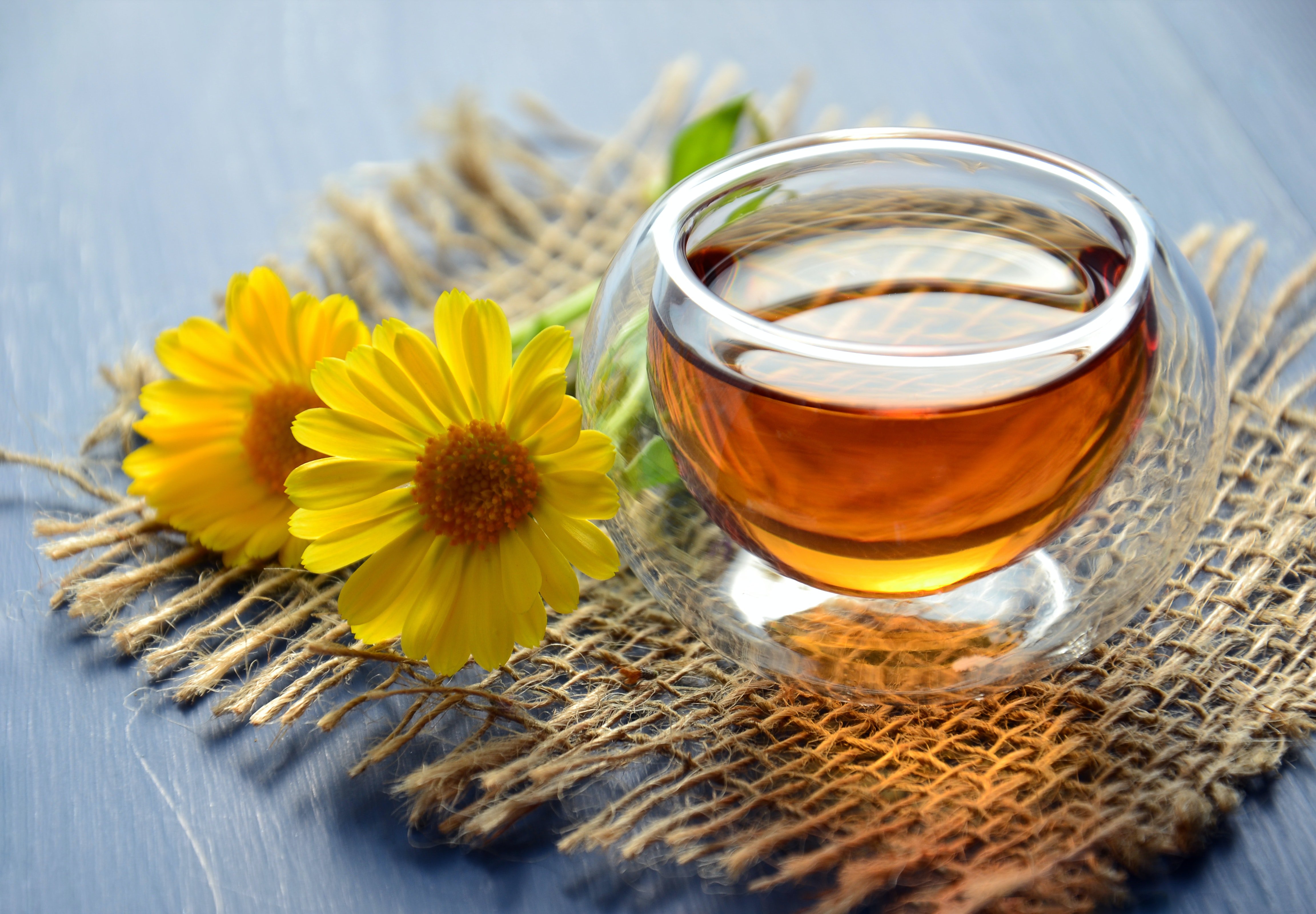 Clear glass mug filled with herbal tea sat on straw patch with yellow flowers