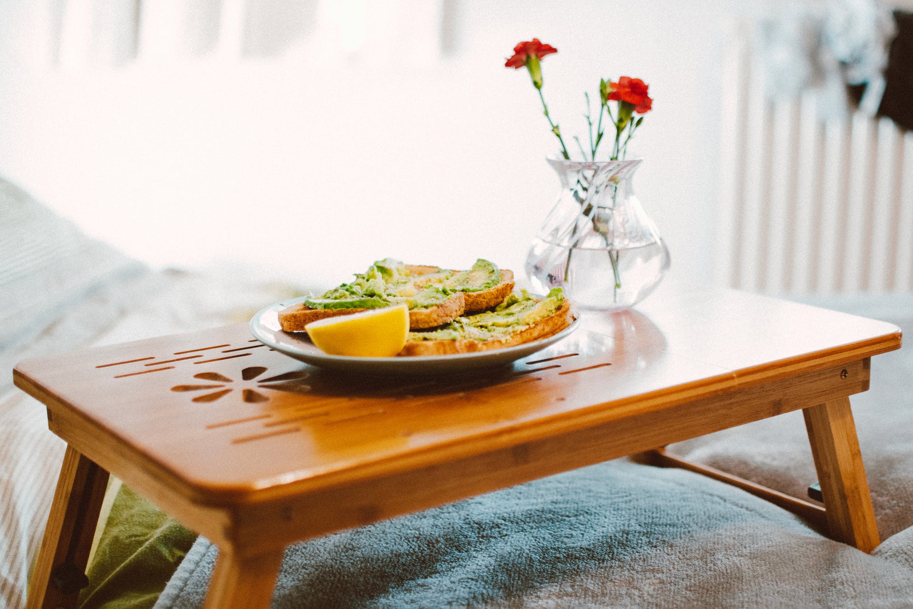 Breakfast in bed, avocado on toast served on wooden tray with vase of flowers 
