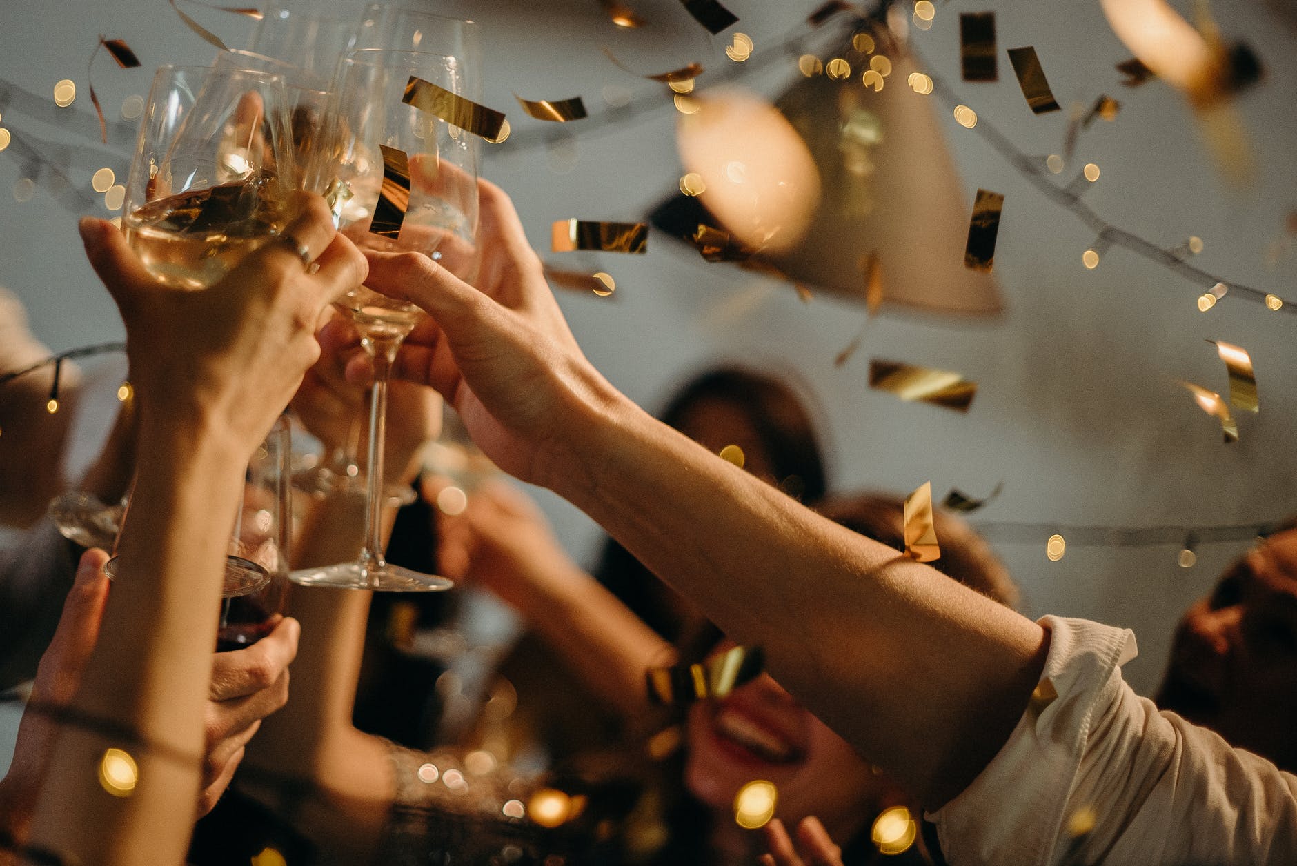 Hands clinking wine glasses at wedding celebration surrounded by gold confetti 