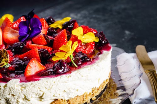 Fruit topped cheesecake sat on glass plate with napkin and knife