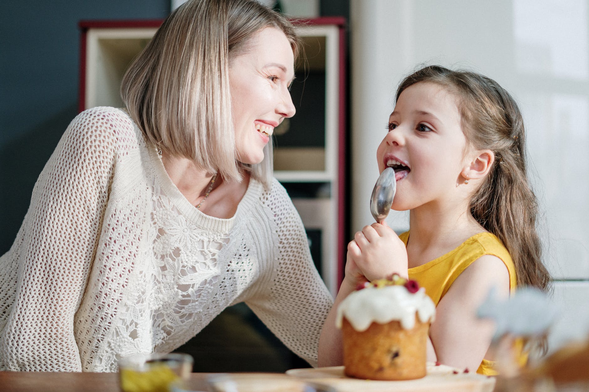Mum laughing as daughter licks a spoon after baking a cake