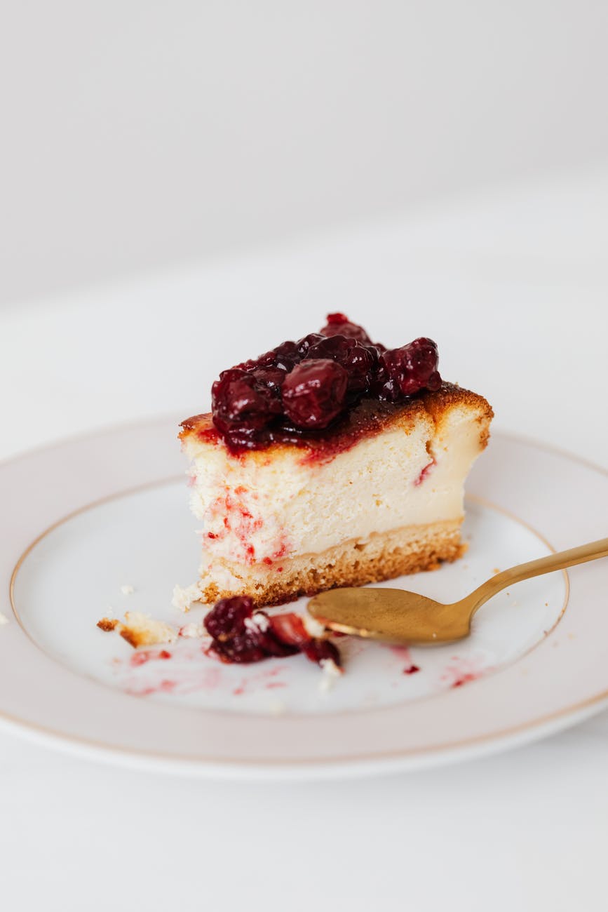 Slice of cheesecake with fruit topping sat on a serving plate with spoon