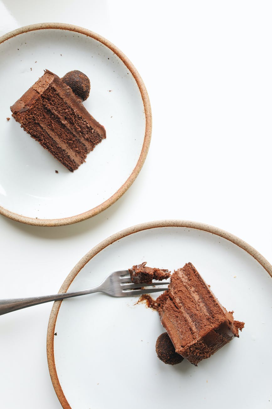 Two white plates with slices of chocolate fudge cake and fork