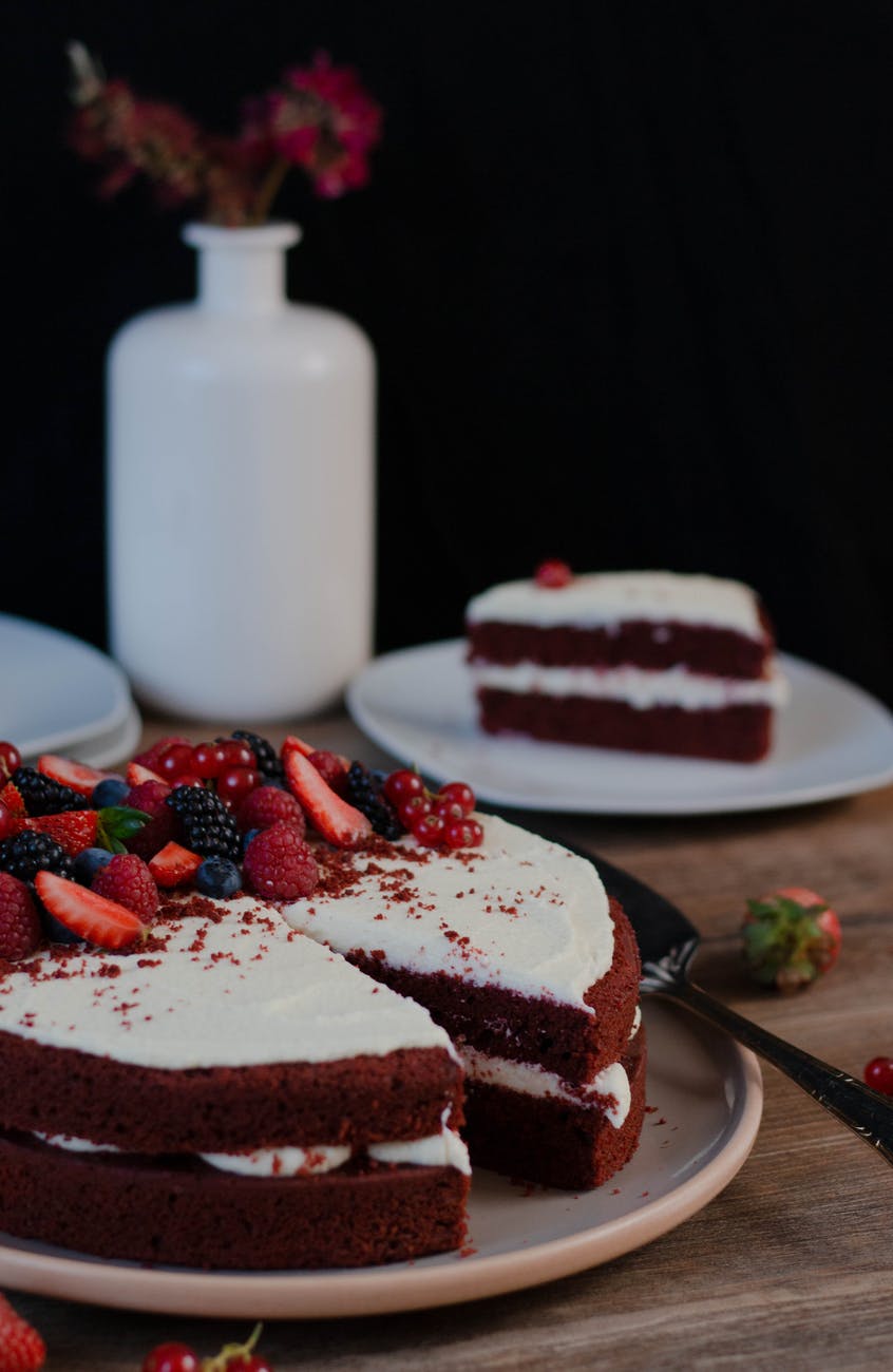 Full red velvet cake with white vase in background