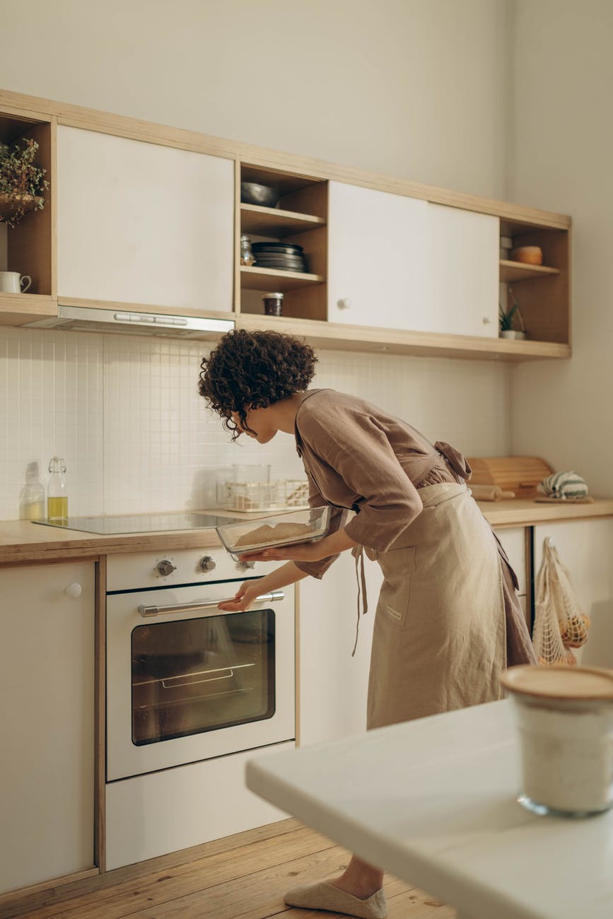 Woman with curly hair and apron in kitchen putting baking in the oven