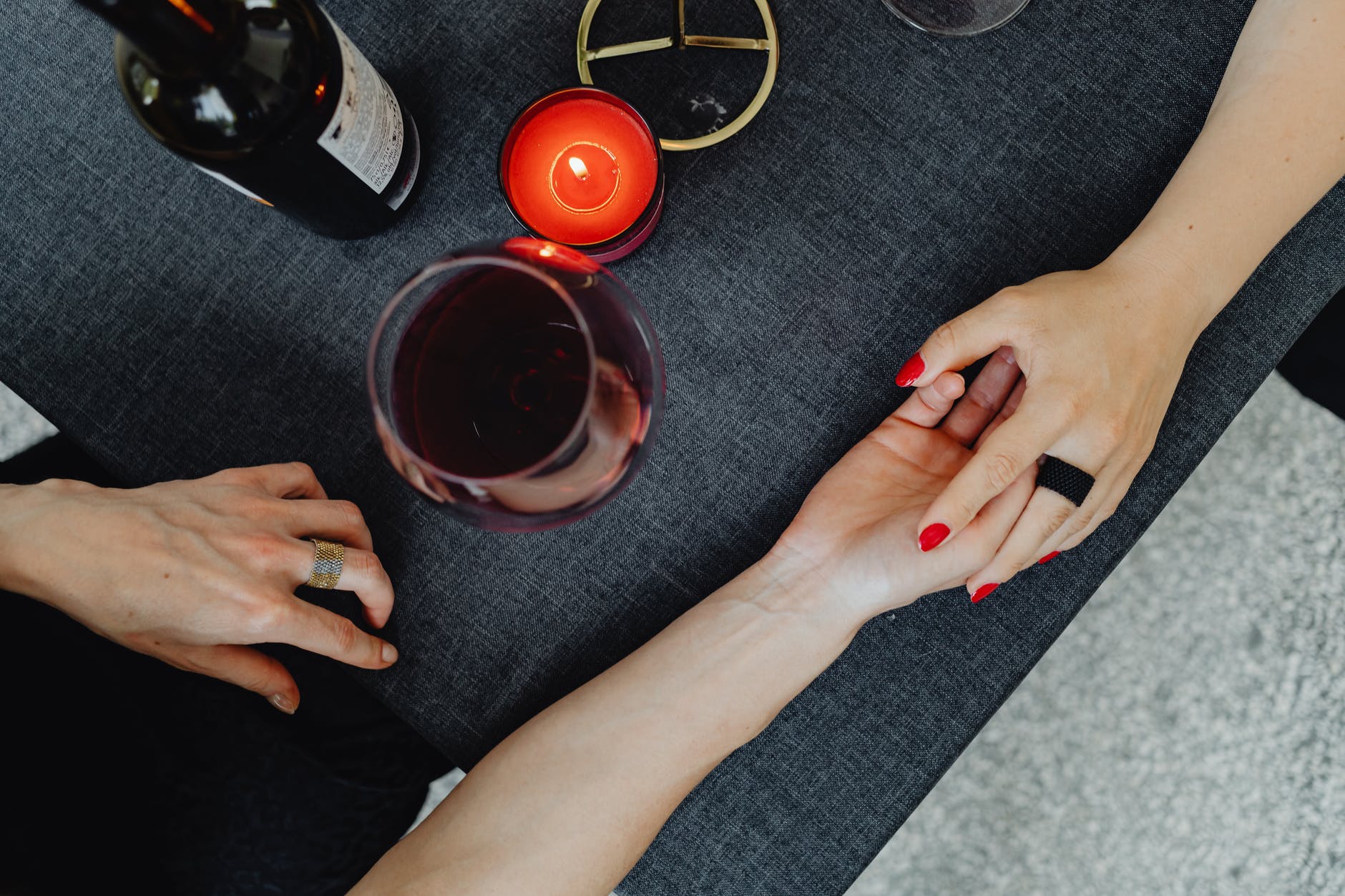 Two women's holding hands across dinner table with candle and bottle of wine