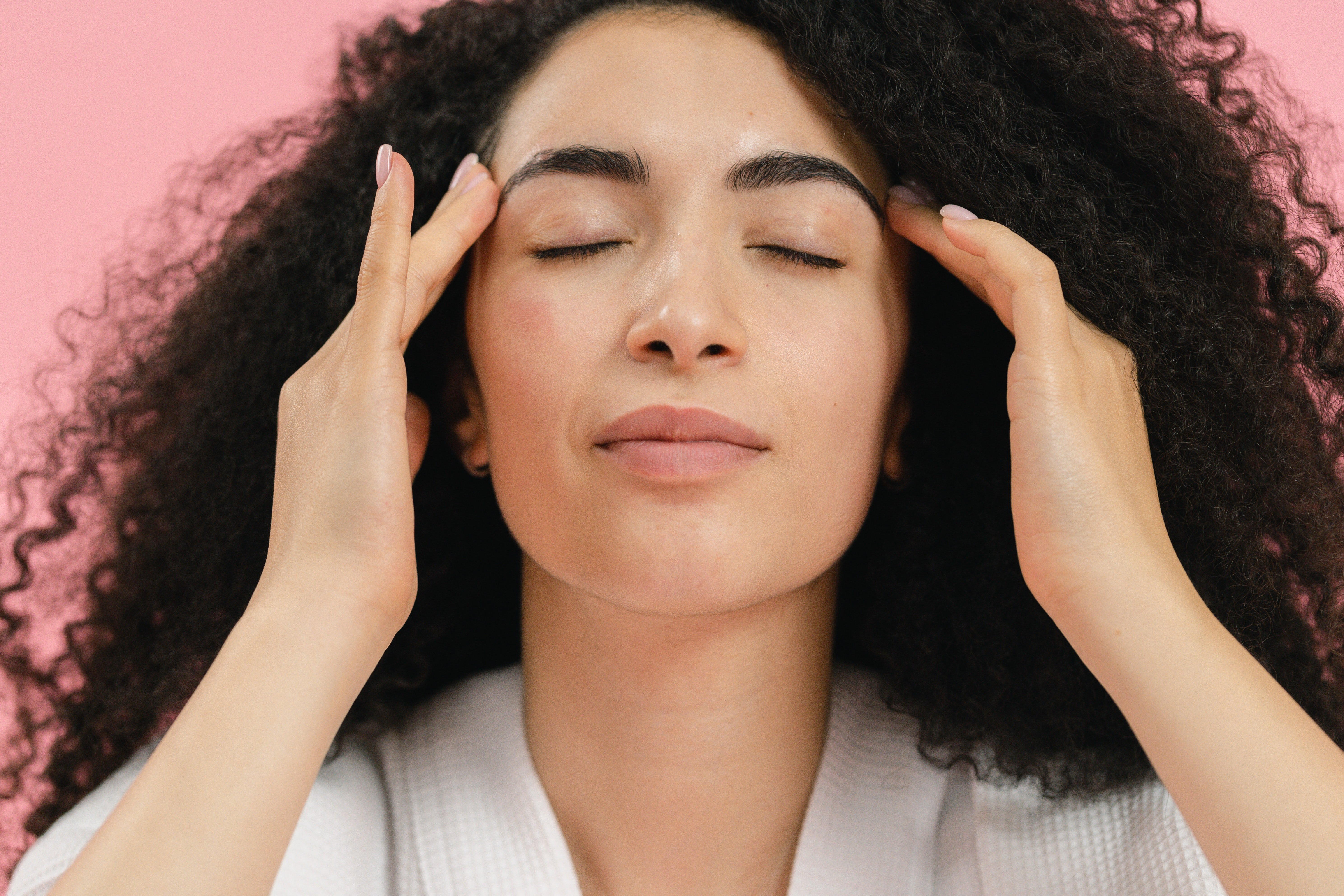 Woman with brown curly hair in robe giving herself head massage