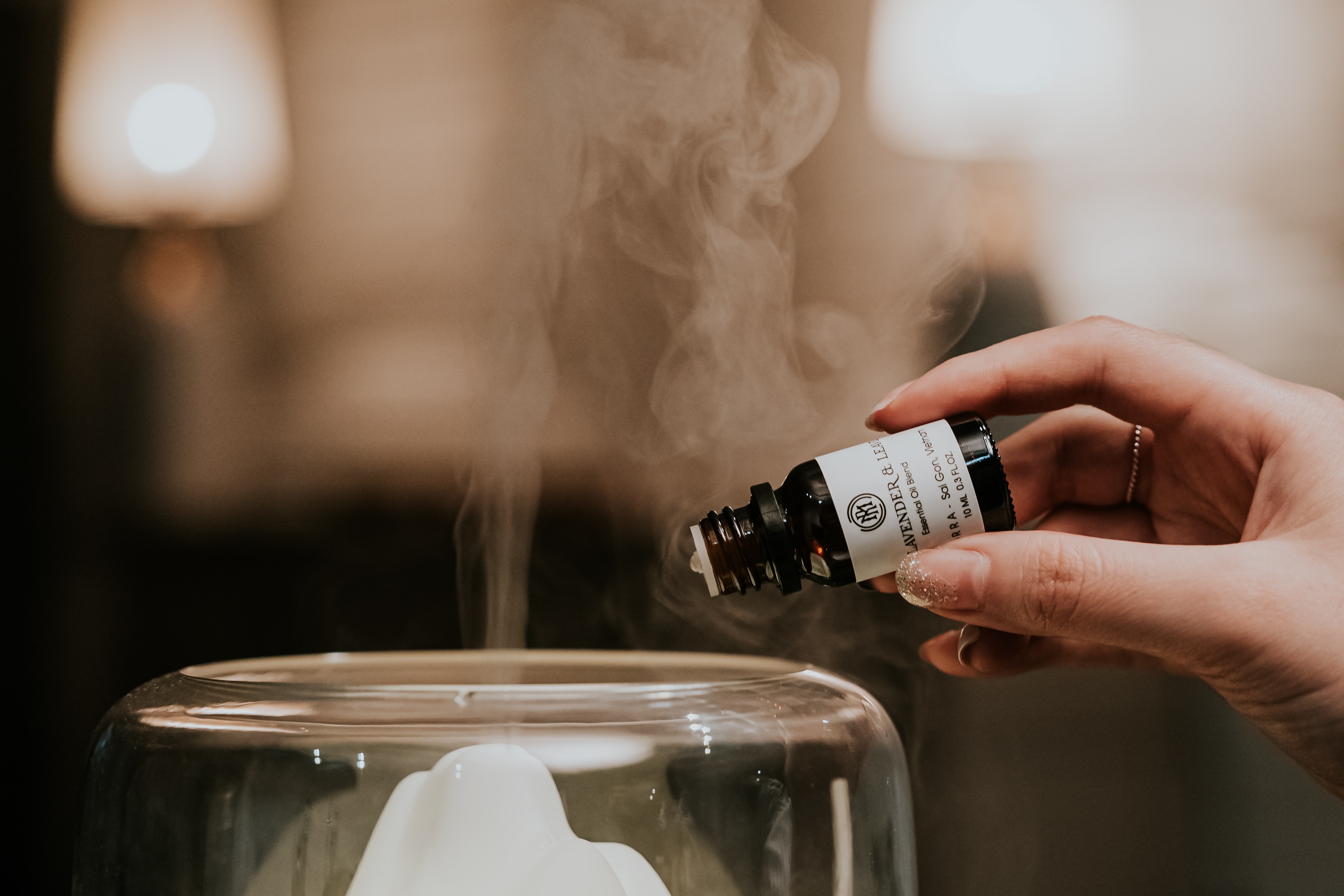 Person pouring lavender essential oils into diffuser for home spa