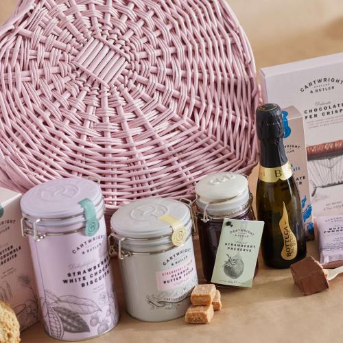 Lifestyle image of From the Heart Hamper - a Pink Heart Shaped Wicker Basket and a collection of Treats including Biscuits, Fudge, Strawberry preserve, Chocolate biscuits, Hot chocolate and Prosecco
